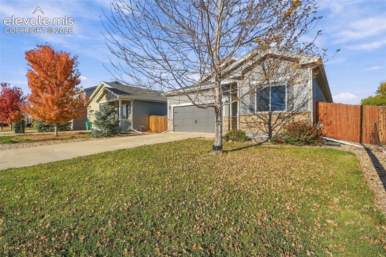 Single-story residence featuring horizontal lap siding, stone veneer accents, an attached garage, and a wood privacy fence
