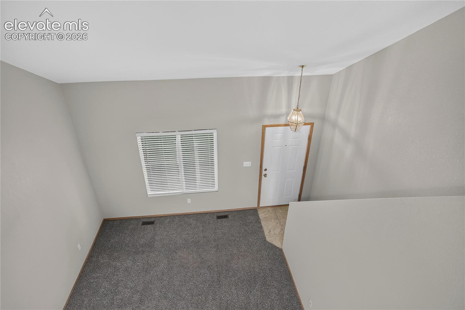 Vaulted ceiling with an overhead light fixture, light gray walls, and dark gray carpet