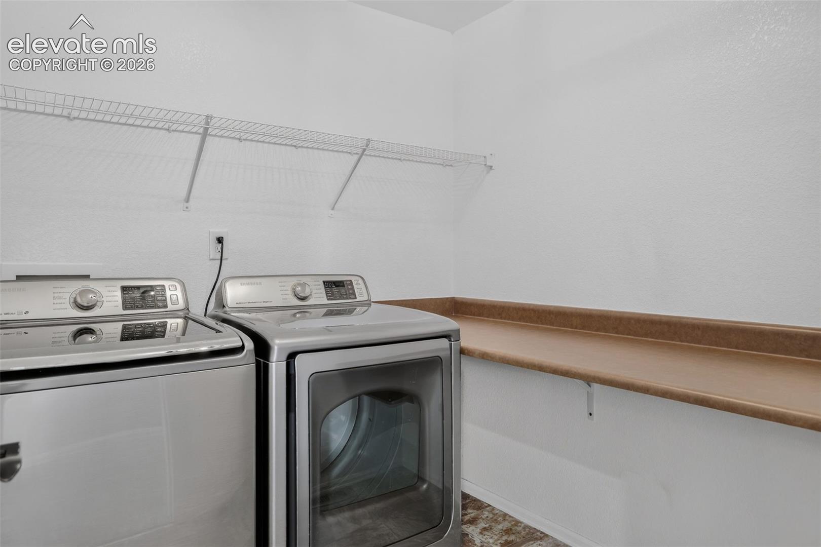 Dedicated laundry space featuring a wire shelf, countertop, and white walls