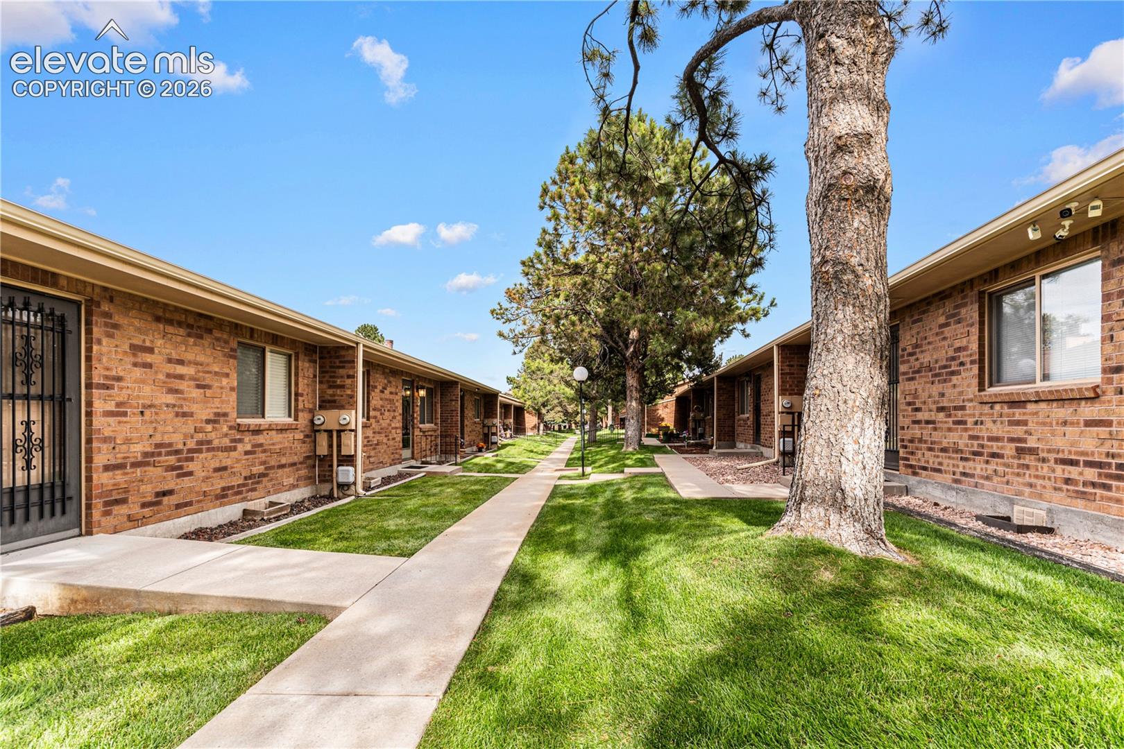 Red brick exterior featuring single-story construction, concrete walkways, green lawns, and mature trees