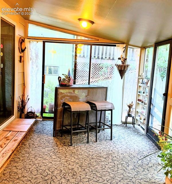 Enclosed sunroom featuring a patterned carpet, sloped ceiling, and multiple windows
