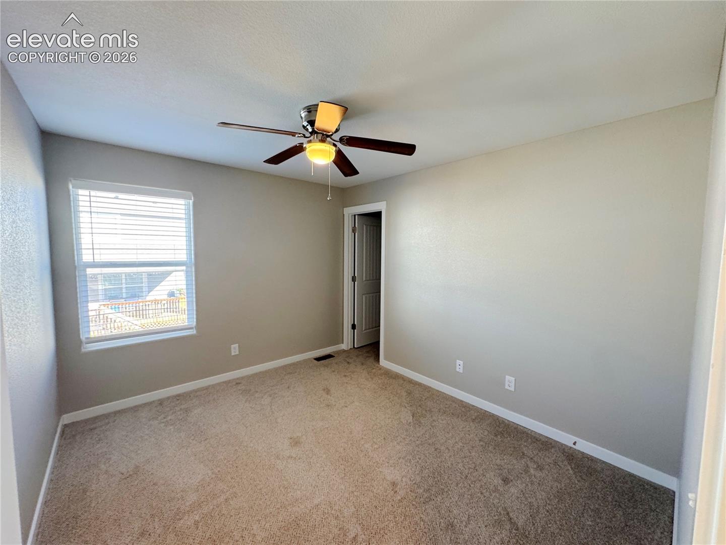 Neutral-toned interior featuring wall-to-wall carpeting, a ceiling-mounted light fixture with fan, and a single-pane window with adjustable horizontal blinds