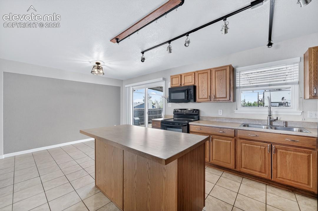 Kitchen featuring a central island, wood-finish cabinetry, tile flooring, a built-in microwave, and a double basin sink