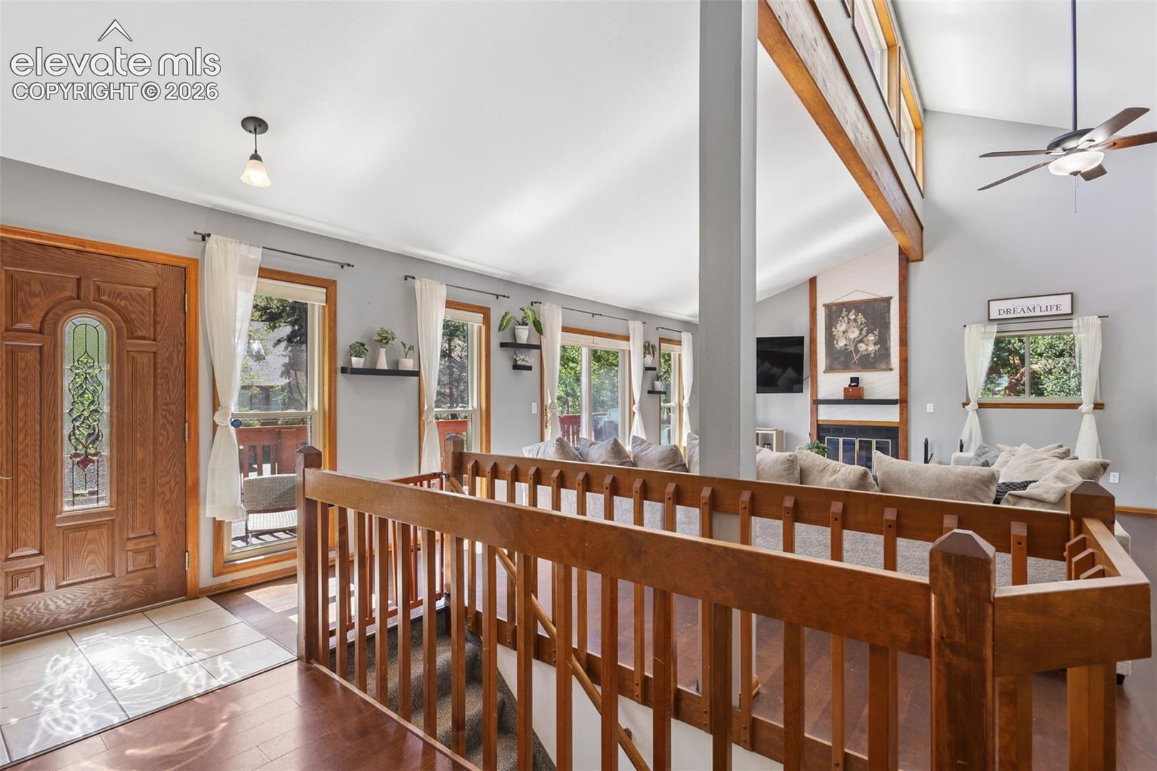 Vaulted ceilings with exposed wood beams, wood-finish flooring, and a fireplace with a stone hearth