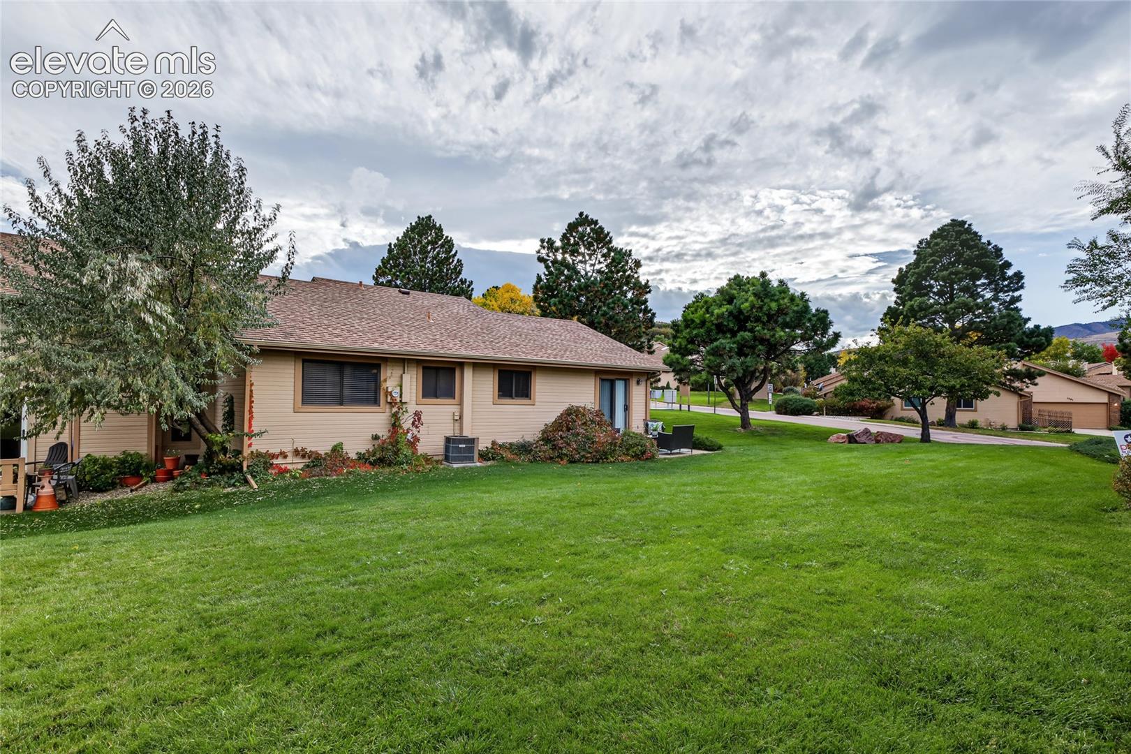 Expansive green lawn with mature trees and a single-story residence featuring a brown shingle roof and tan siding