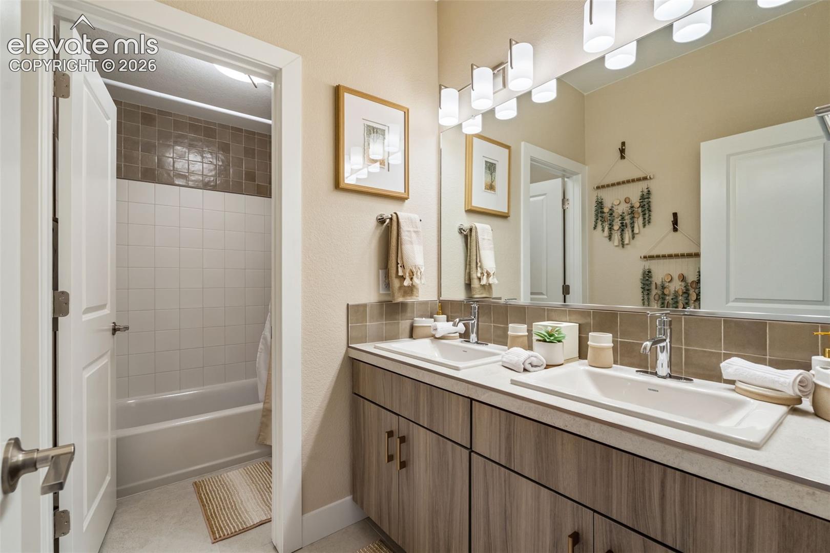 Double vanity featuring wood-finish cabinetry, solid-surface countertops with integrated rectangular sinks, and a large frameless mirror