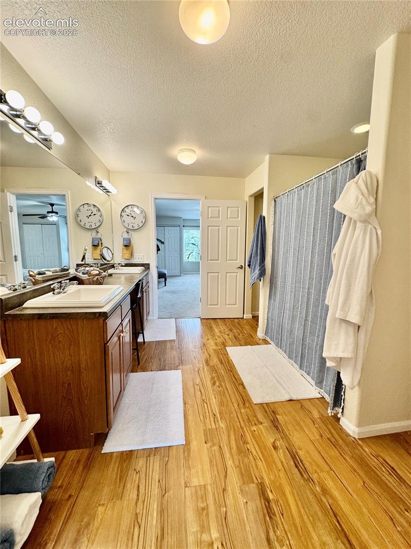 Bathroom featuring wood-finish flooring, a double vanity with ample cabinetry, a large mirror, and a shower area with a privacy curtain