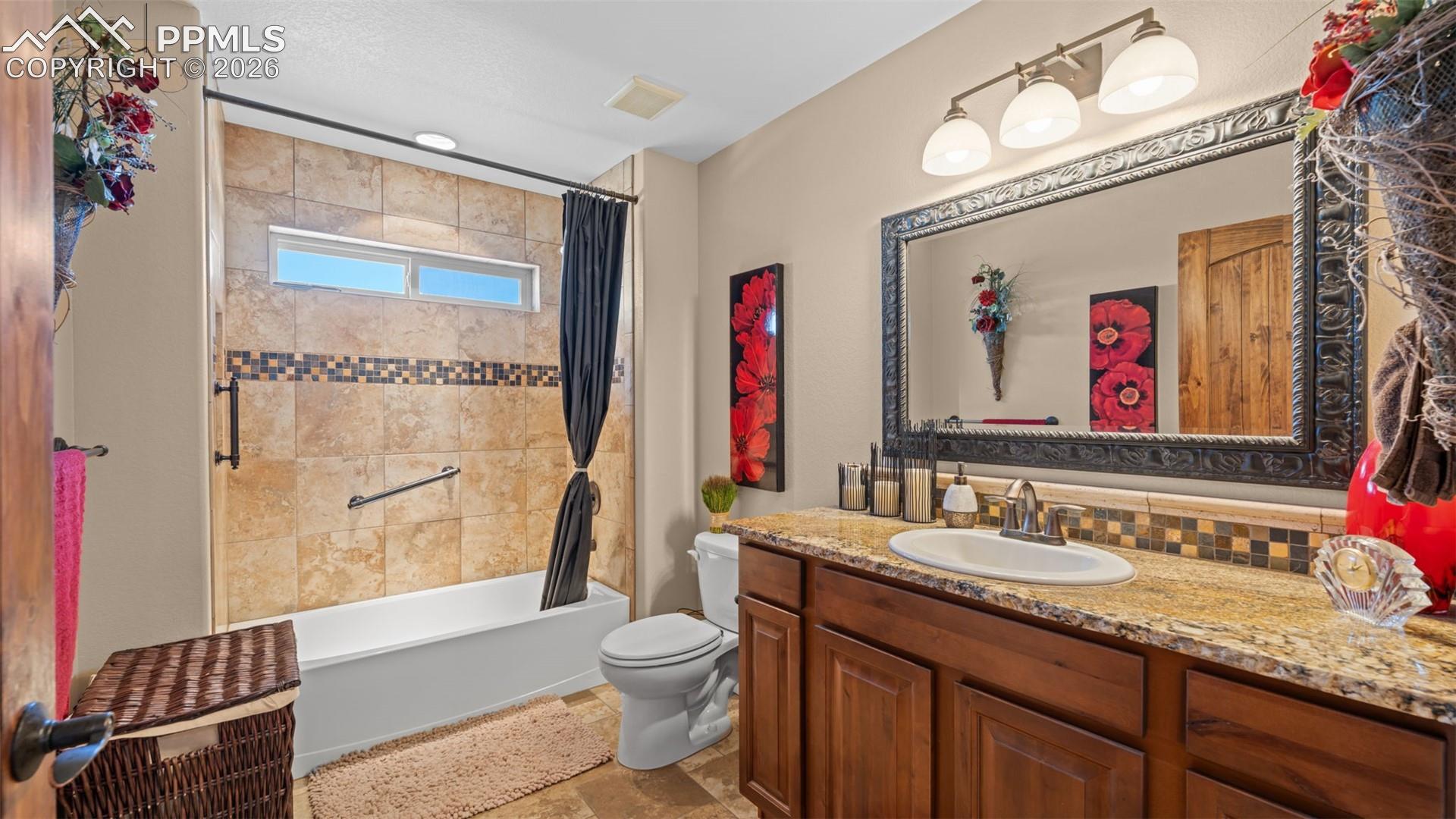 Bathroom featuring vanity, light stone finish flooring, shower / bath combo with shower curtain, and decorative backsplash