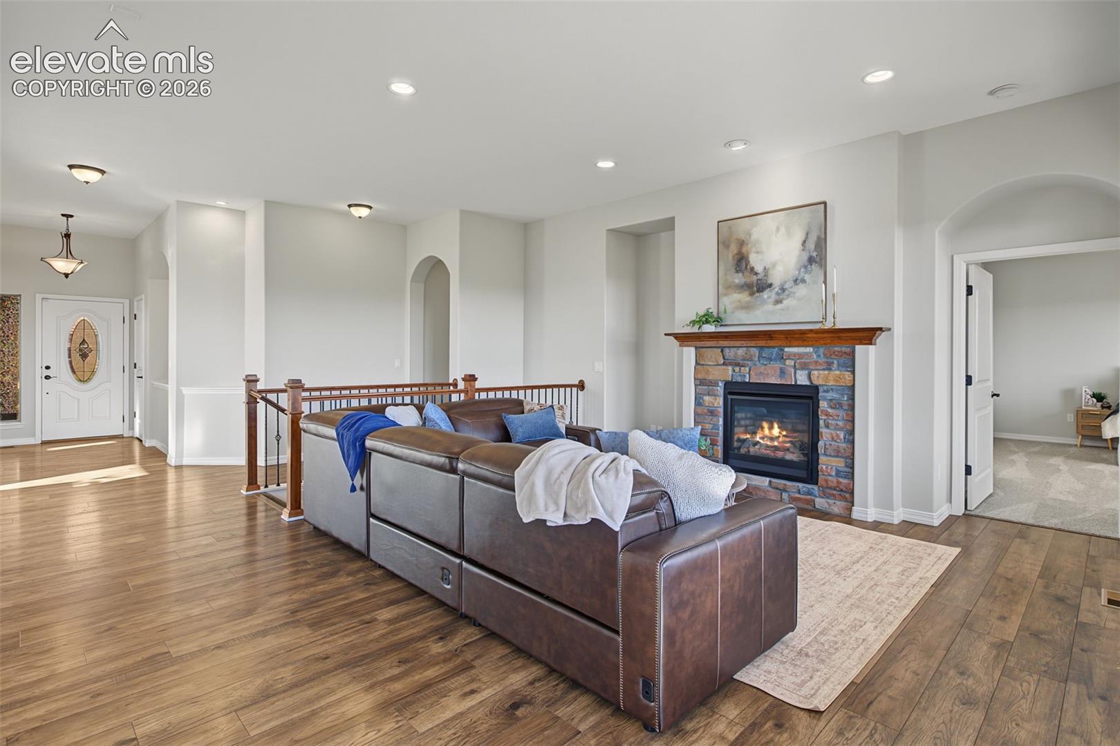 Open floor plan featuring wood-finish flooring, recessed lighting, a stone-surround fireplace with a wood mantel, and arched architectural details