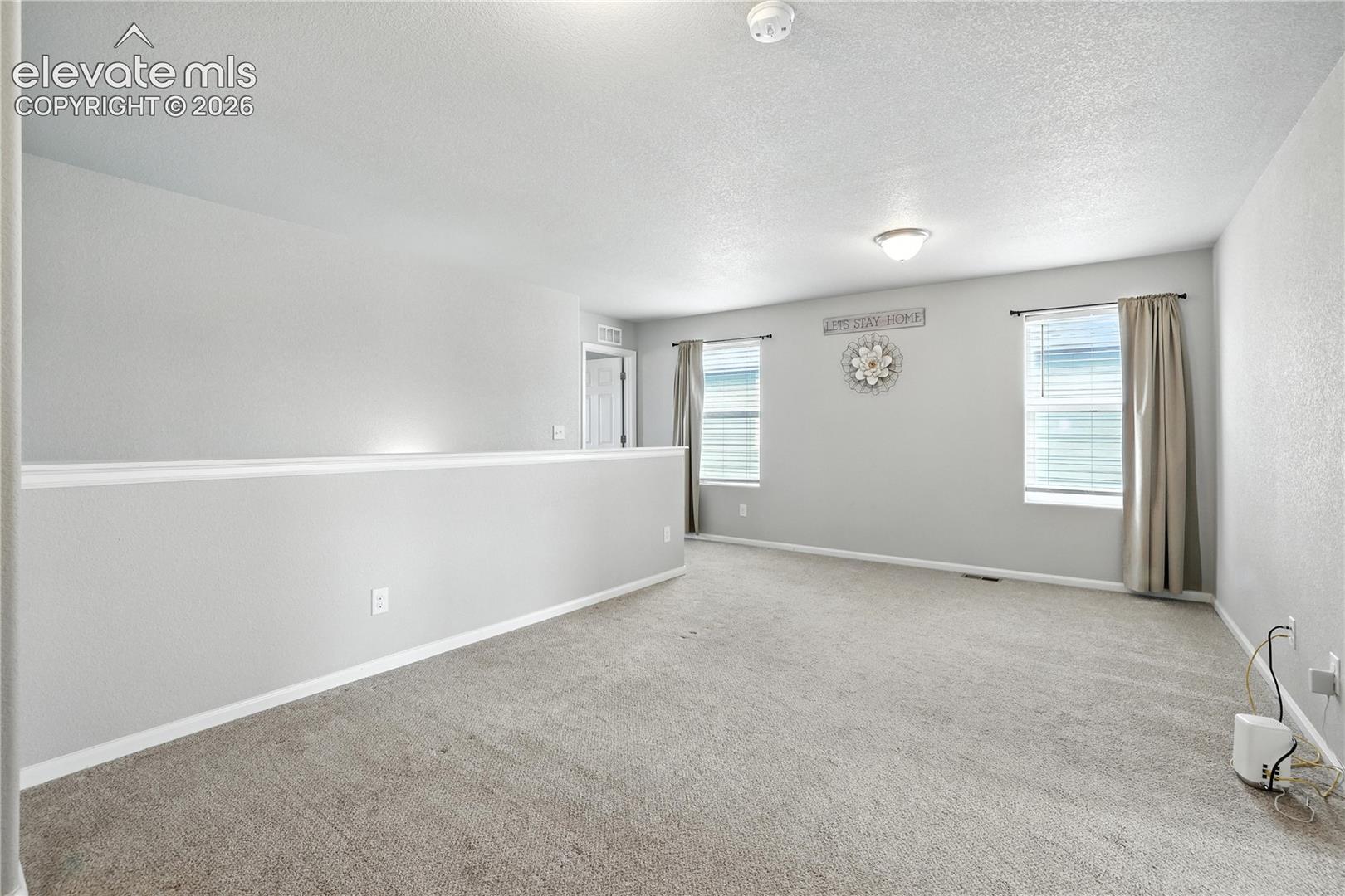 Carpeted flooring, neutral wall color, two windows with blinds, overhead flush mount lighting, and a partial wall with white trim