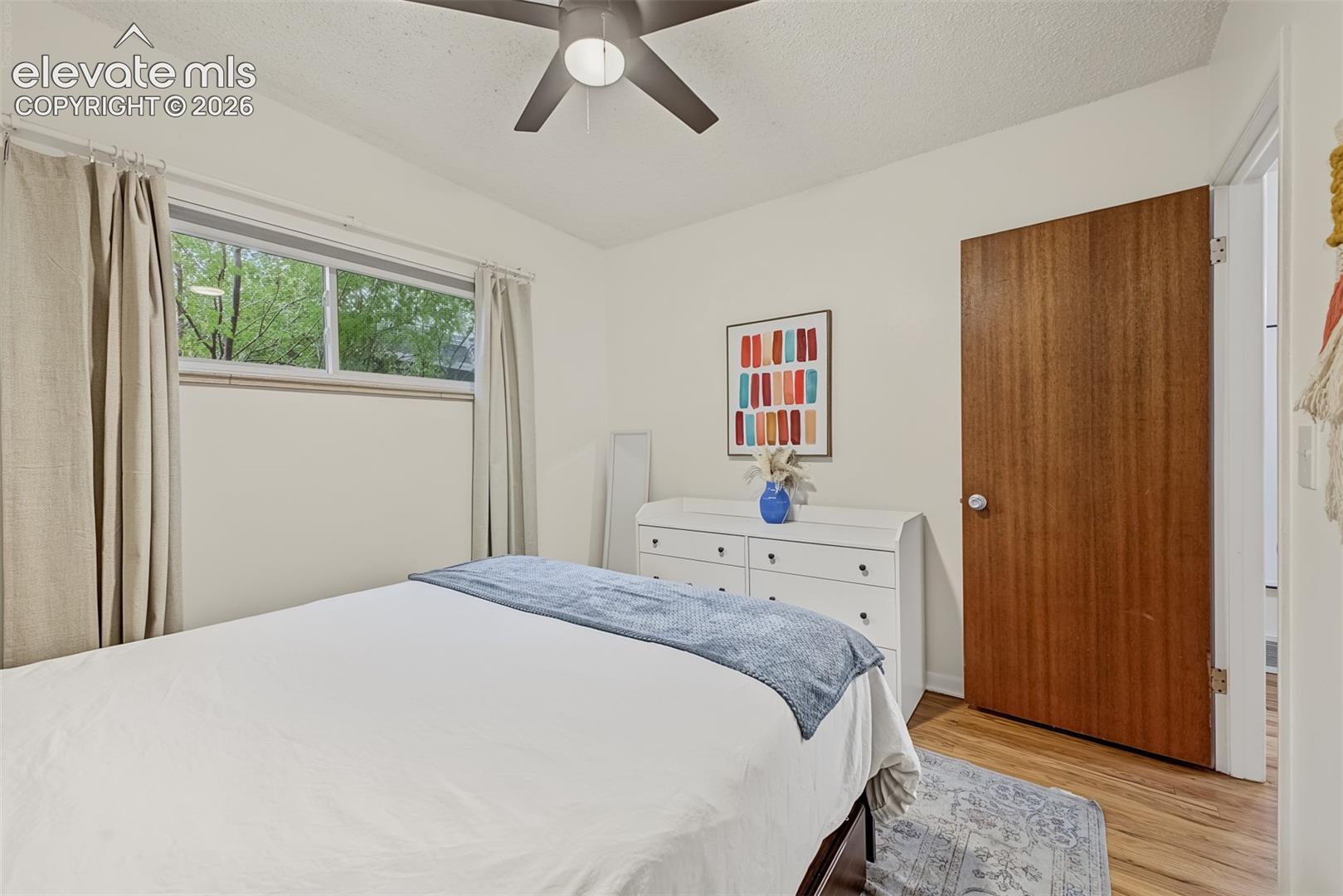 Room featuring wood-finish flooring, a horizontal sliding window, and a ceiling-mounted light fixture with fan blades