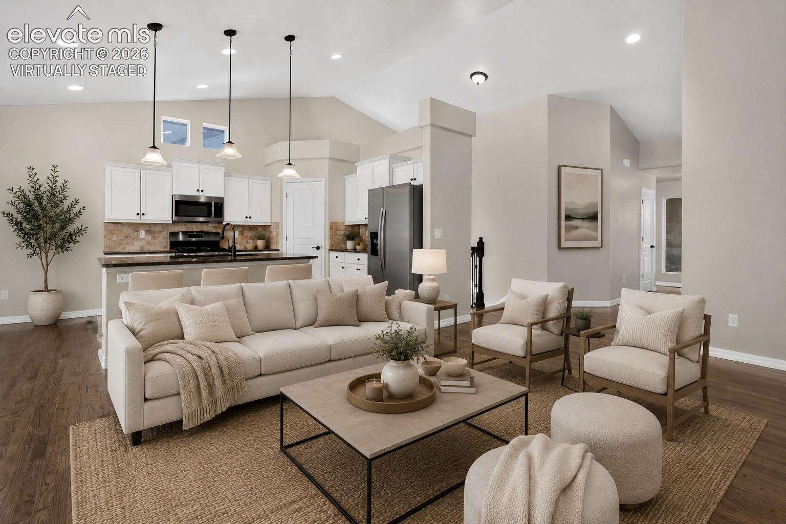 Virtually Staged - Open-concept living space featuring vaulted ceilings, wood-finish flooring, white kitchen cabinetry, a kitchen island with pendant lighting, and recessed lighting