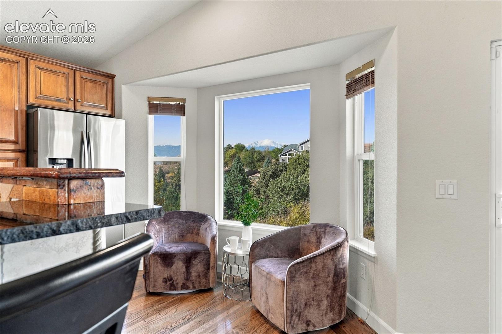 Bay window with mountain scenery, wood-finish flooring, dark stone-surfaced breakfast bar, and upper wood cabinetry