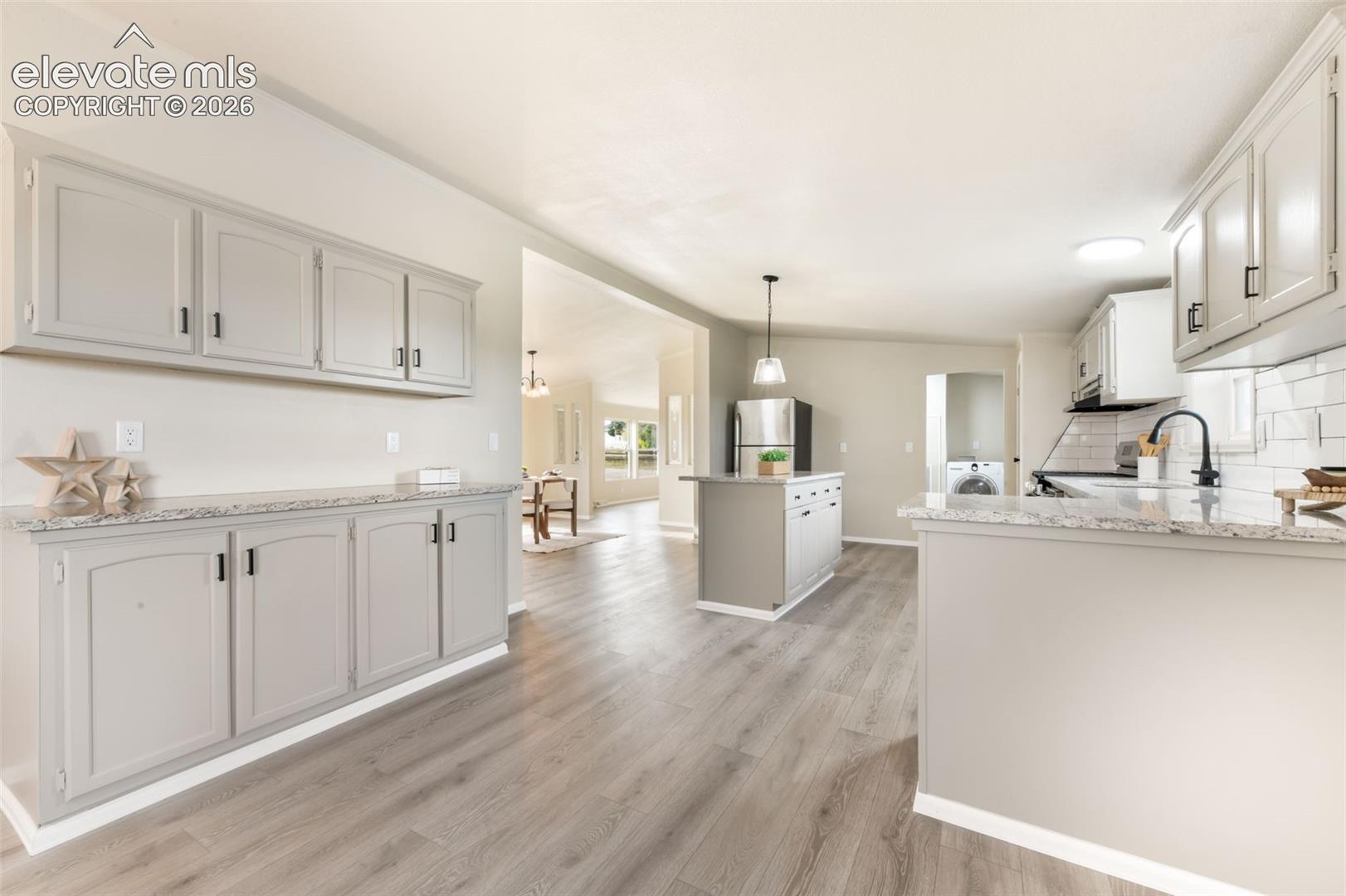Open concept kitchen featuring gray cabinetry, granite countertops, white subway tile backsplash, and wood-finish flooring