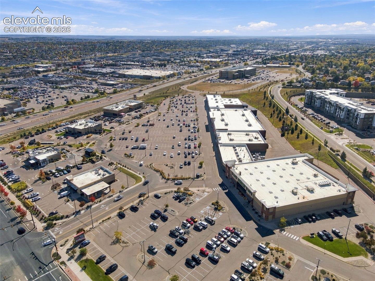 Aerial view of shopping and commercial plaza just monutes away featuring paved parking areas, multi-tenant building structures, flat roofing, and proximity to major roadway infrastructure