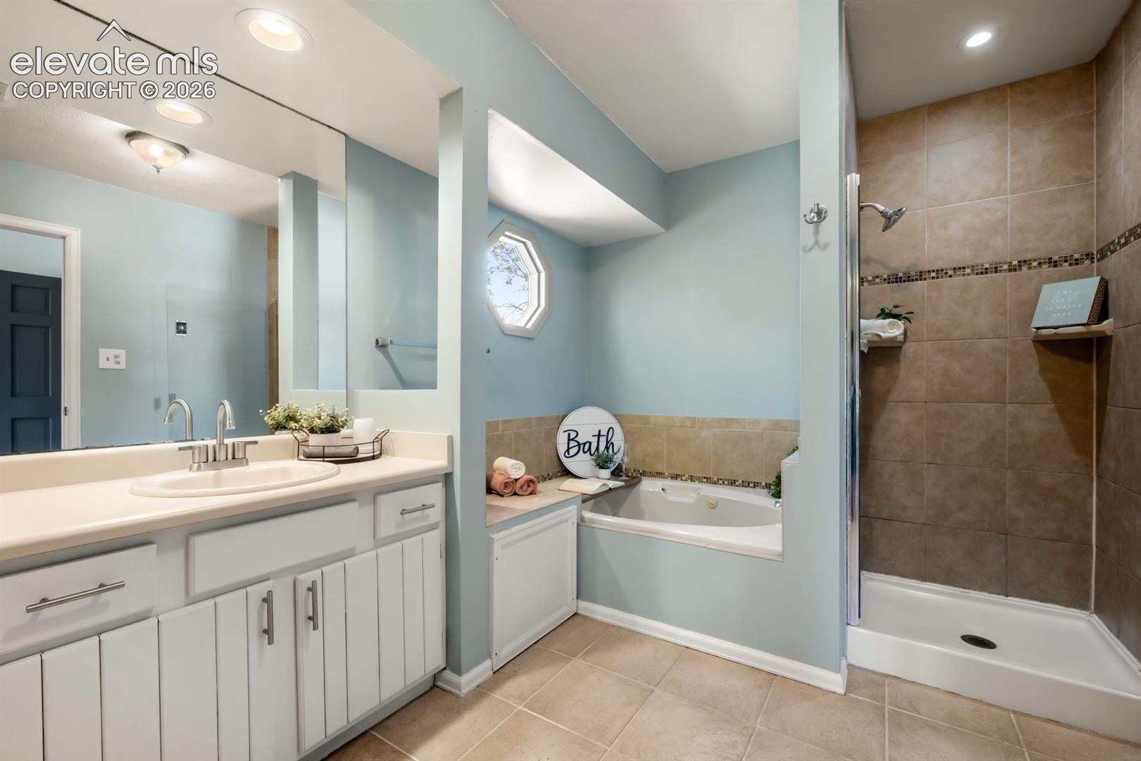 Bathroom featuring a vanity with a large mirror, a built-in tub with an octagonal window, and a tiled shower stall