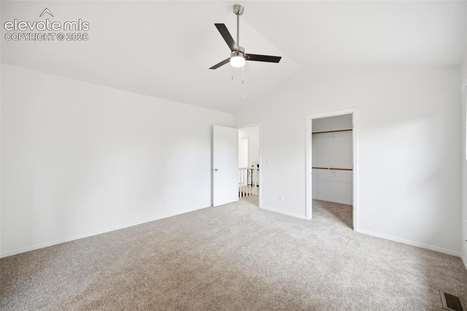 Vaulted ceilings, neutral carpeting, and a ceiling fan with integrated lighting, featuring a walk-in closet with built-in shelving