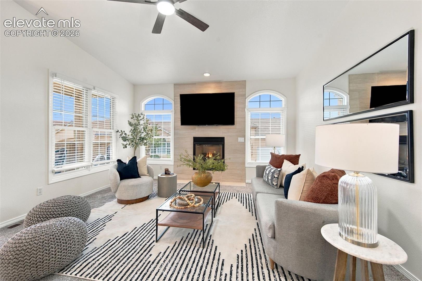 Living area featuring a floor-to-ceiling tile fireplace surround, vaulted ceilings, arched windows, recessed lighting, and a ceiling fan