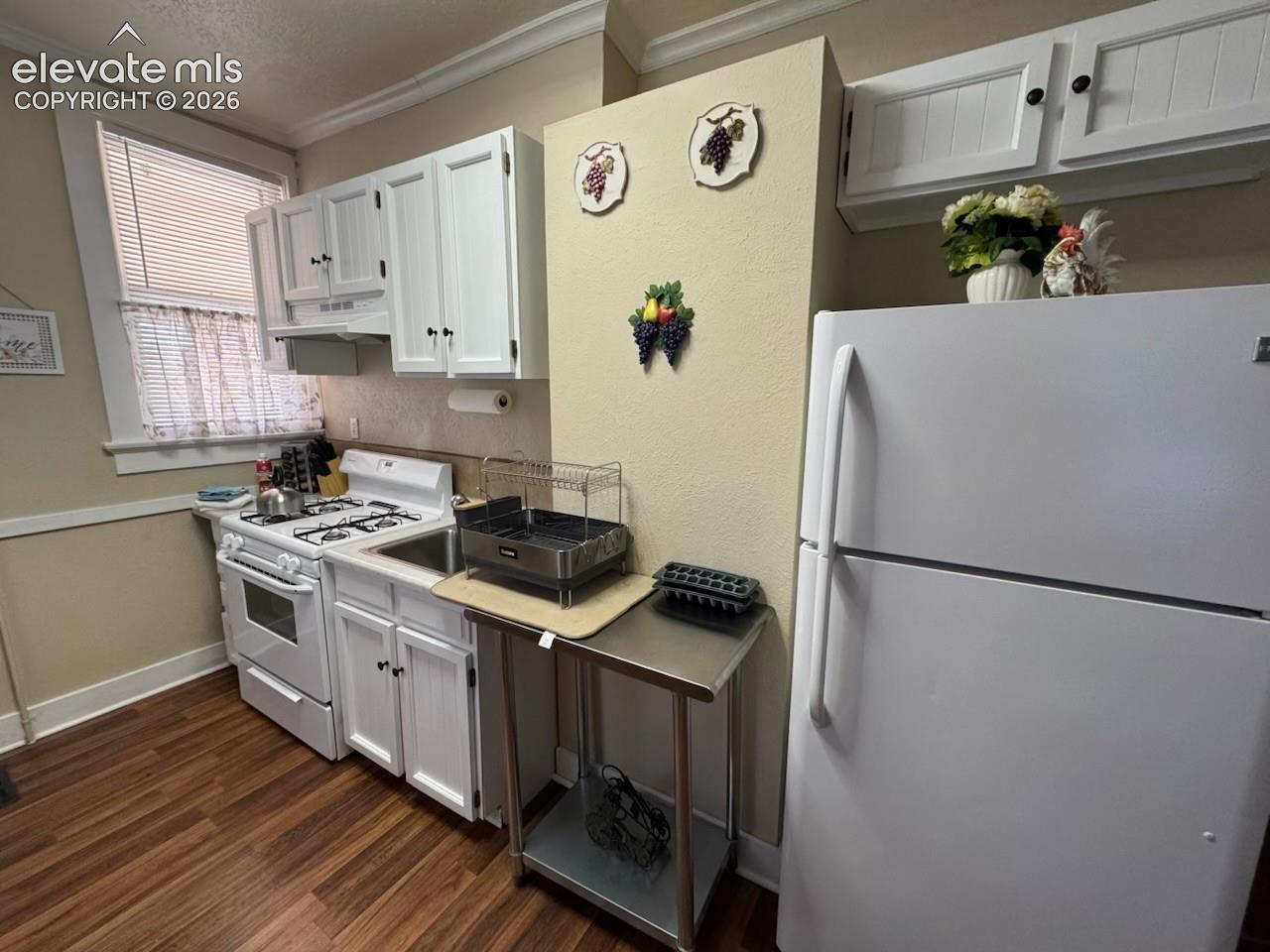 White cabinetry with black hardware, wood-finish flooring, white gas range with oven, window with blinds, and a built-in kitchen sink
