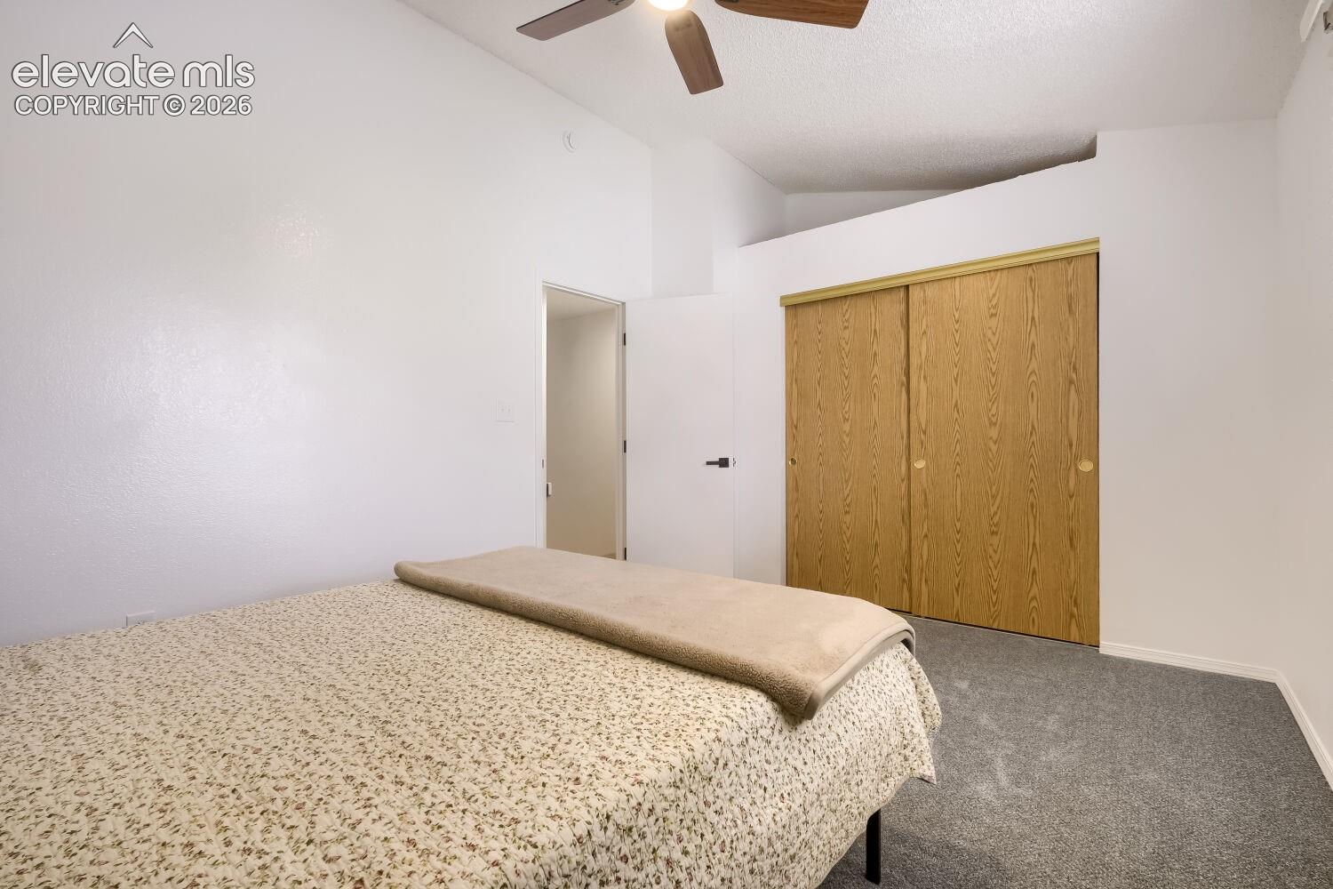 Room featuring vaulted ceilings, a ceiling fan with integrated lighting, wall-to-wall carpeting, and a dual-panel sliding closet