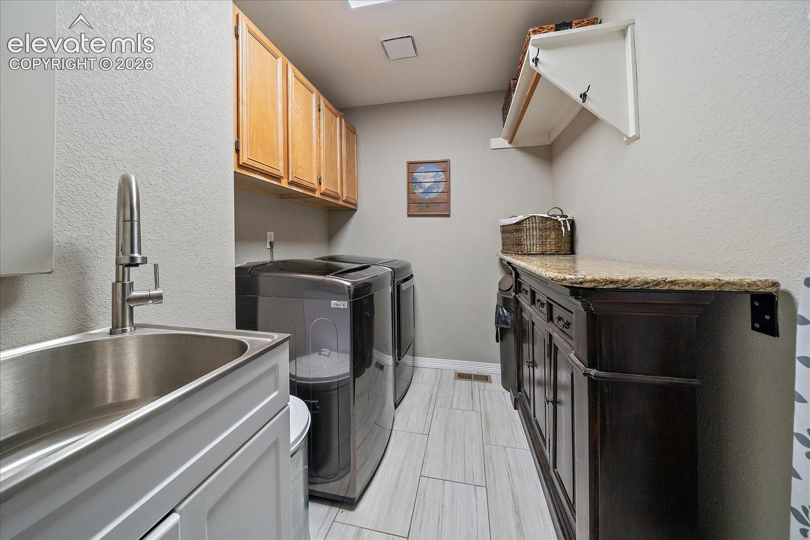 Laundry room featuring wood-finish wall cabinetry, a stone-surfaced built-in counter, a stainless steel sink with a high-arch faucet, and tile flooring