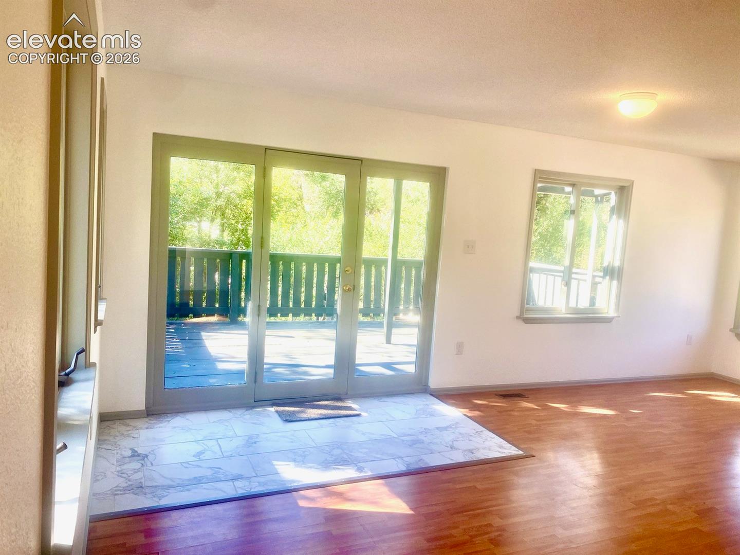 Patio doors opening to an exterior deck, complemented by wood-finish flooring and a tiled entry