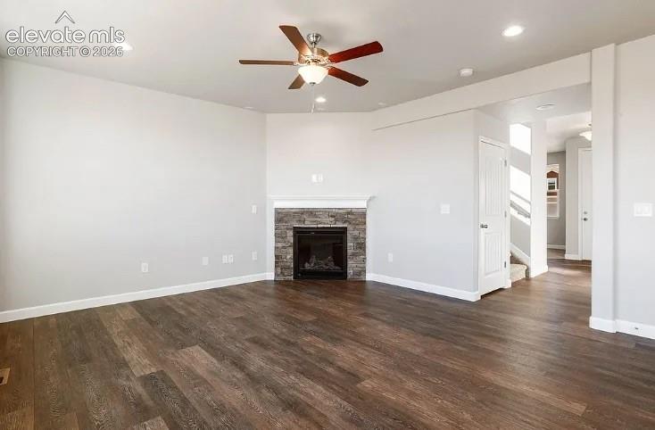Living area featuring wood-finish flooring, a stone-surround fireplace, a ceiling fan with integrated lighting, and recessed ceiling lights