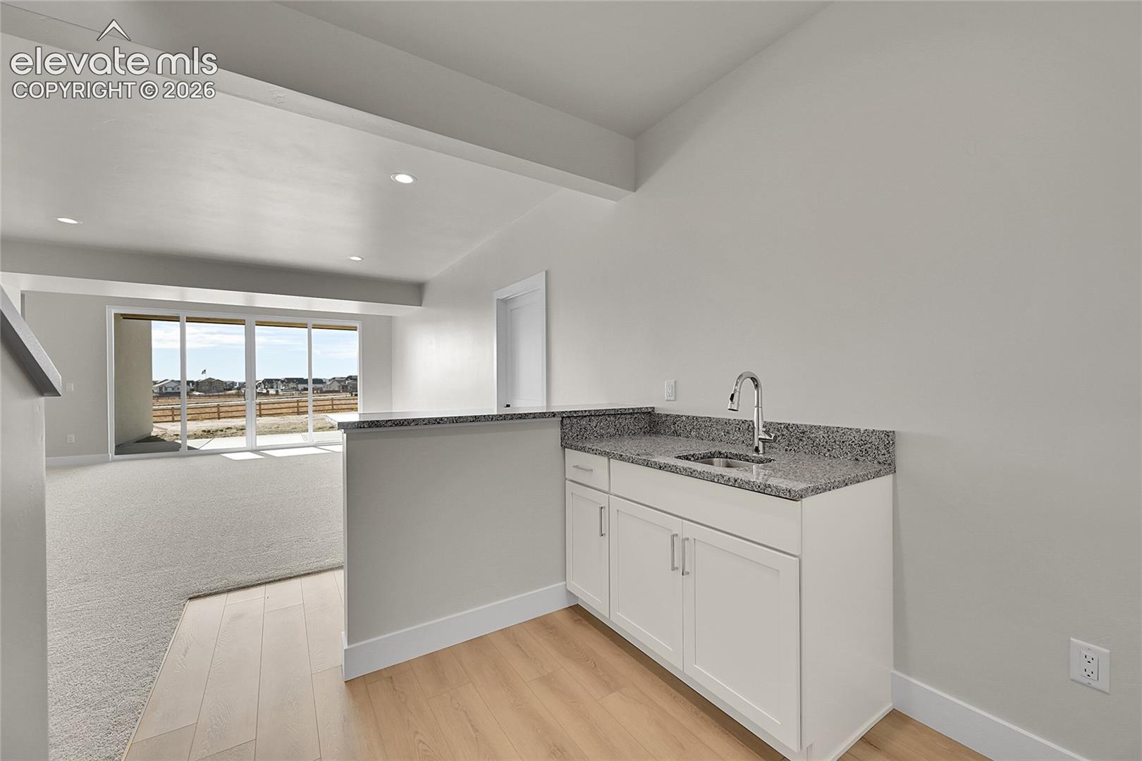Built-in wet bar featuring white cabinetry, a granite countertop, and a stainless steel sink with a single-handle faucet