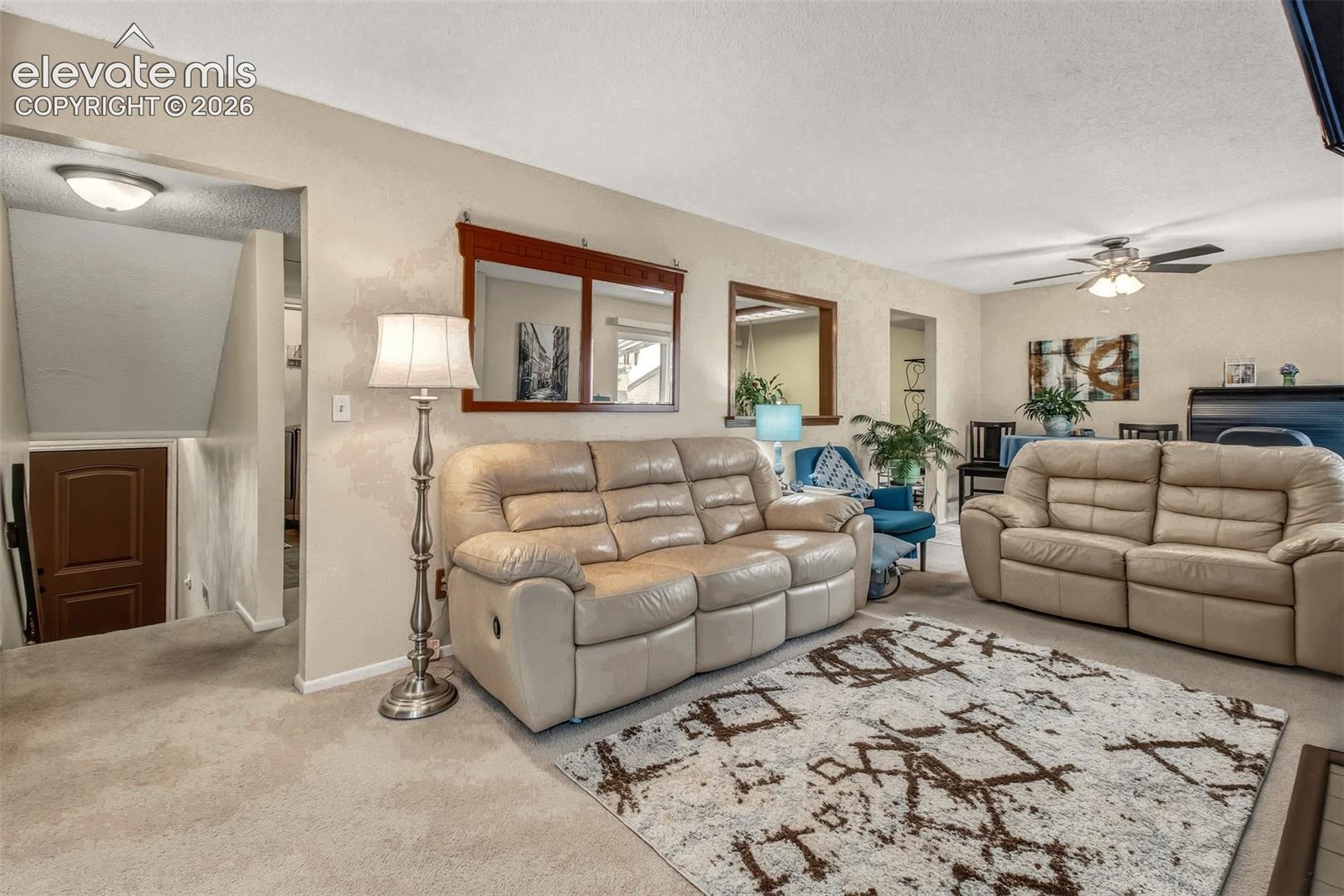 Neutral interior featuring light carpeting, wall-mounted wood-trimmed mirrors, interior pass-through window, and a ceiling fan with integrated lighting
