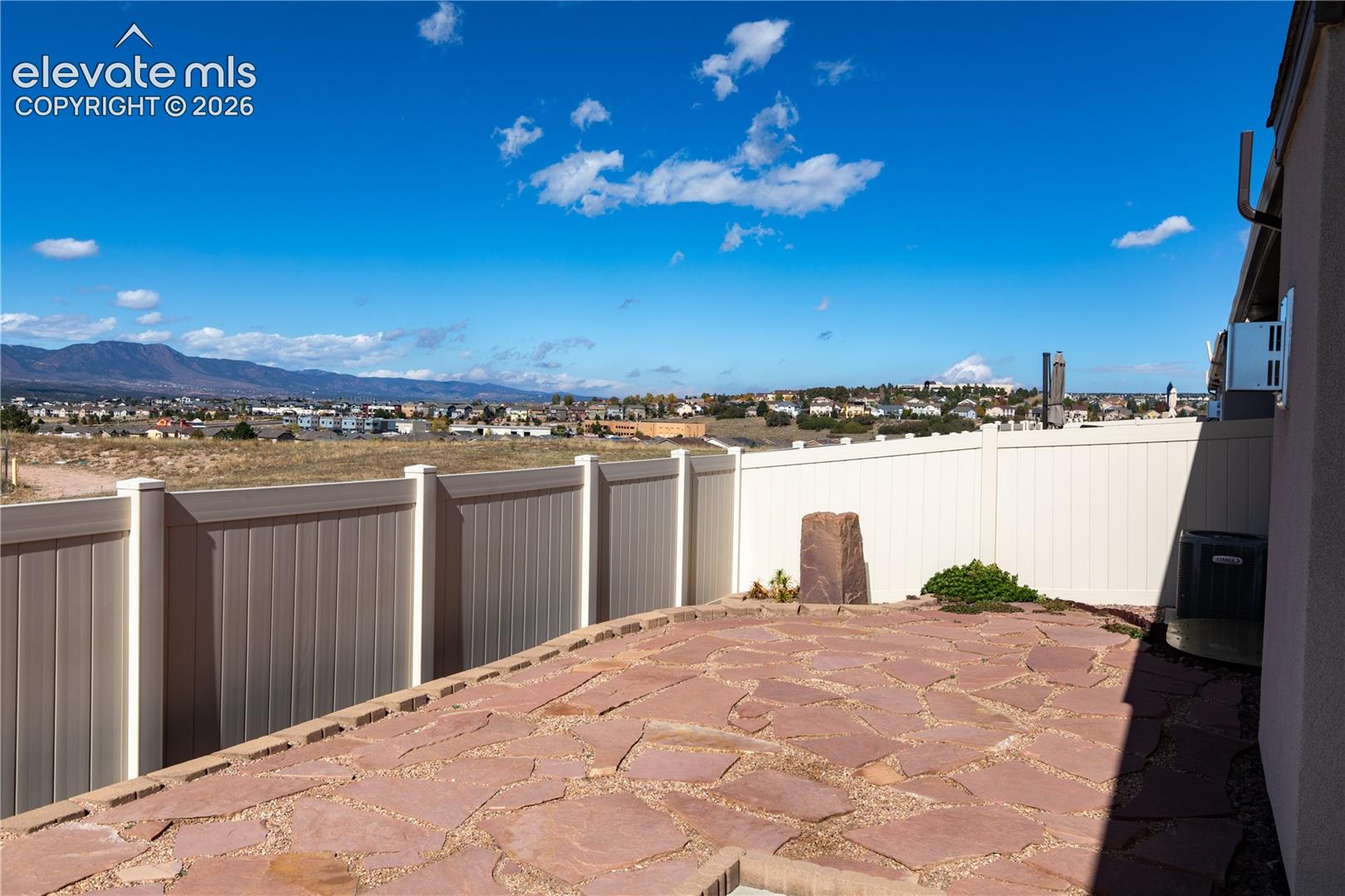 Flagstone patio enclosed by a white vinyl privacy fence, featuring a prominent mountain backdrop