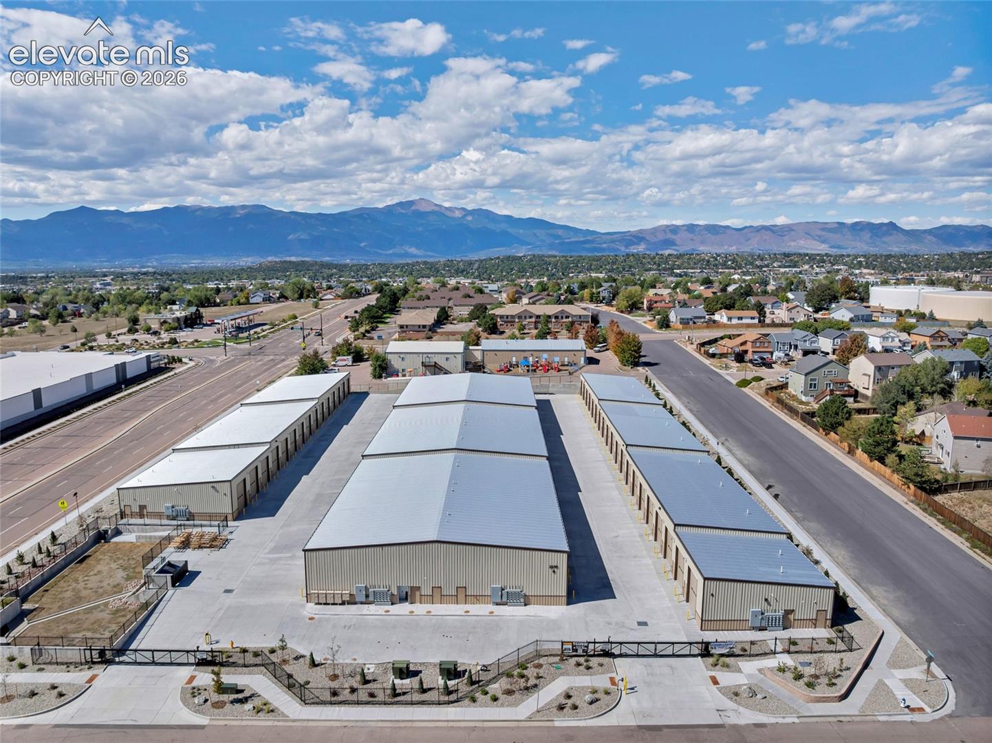 Multiple storage buildings with metal roofs, paved access roads, and fenced perimeters