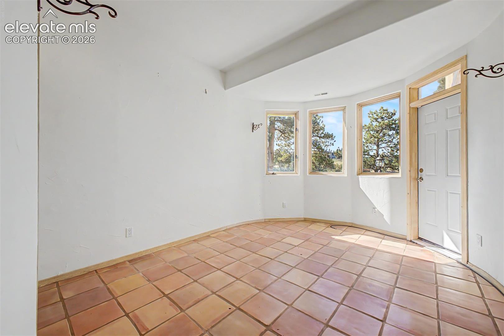 Terracotta tile flooring, three large windows, white paneled door, and white walls