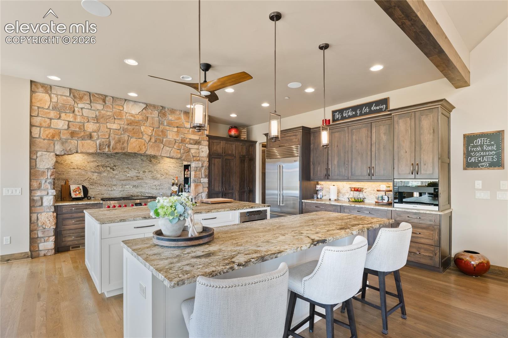 A chef's dream with a designer's eye. Custom culinary kitchen featuring a 48-inch Wolf 6-burner range, Sub-Zero refrigerator, built-in Miele coffee and espresso system, full-slab leathered granite, dual 9-foot prep and seating islands, and a dramatic floor-to-ceiling stone accent wall.