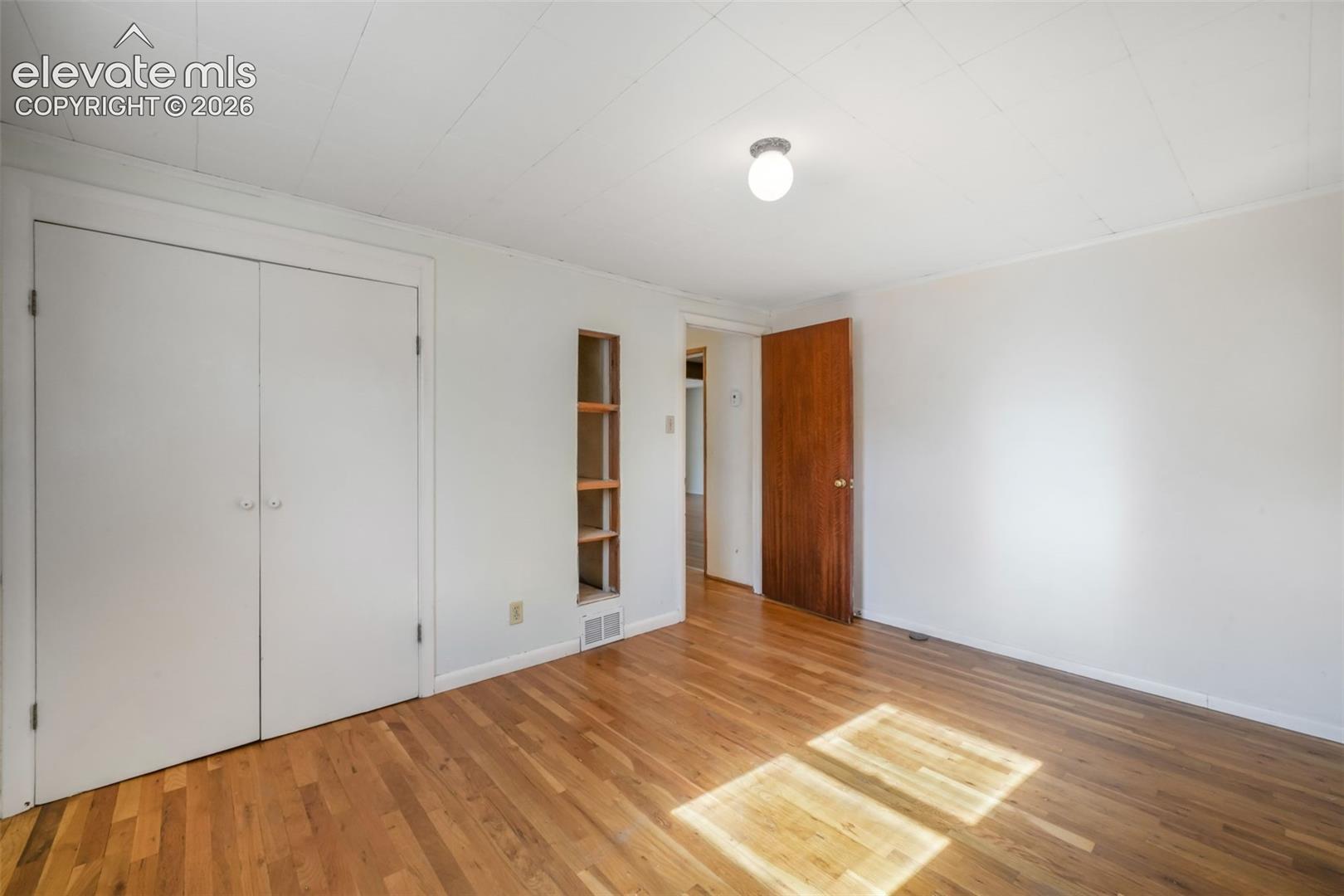 Hardwood flooring, built-in shelving, flush mount ceiling light, and white paneled bi-fold closet doors