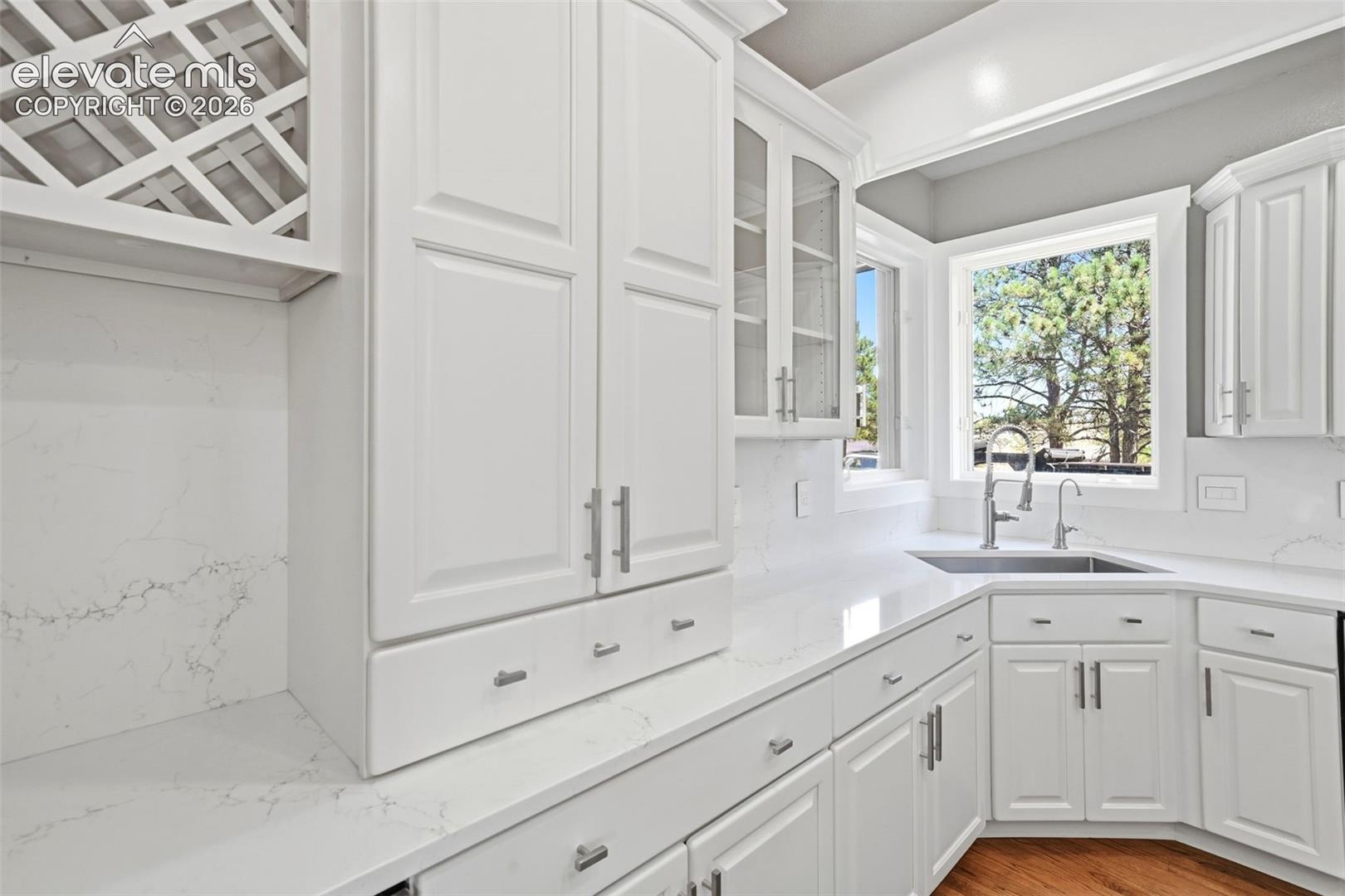 Kitchen featuring white shaker-style cabinetry, a built-in wine rack, light-toned countertops, a stainless steel sink with a gooseneck faucet, and a large bay window