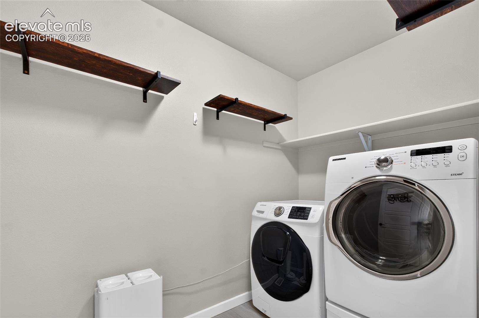 Dedicated laundry area with a white shelving unit, wood-finish wall shelves, and light gray wall paint