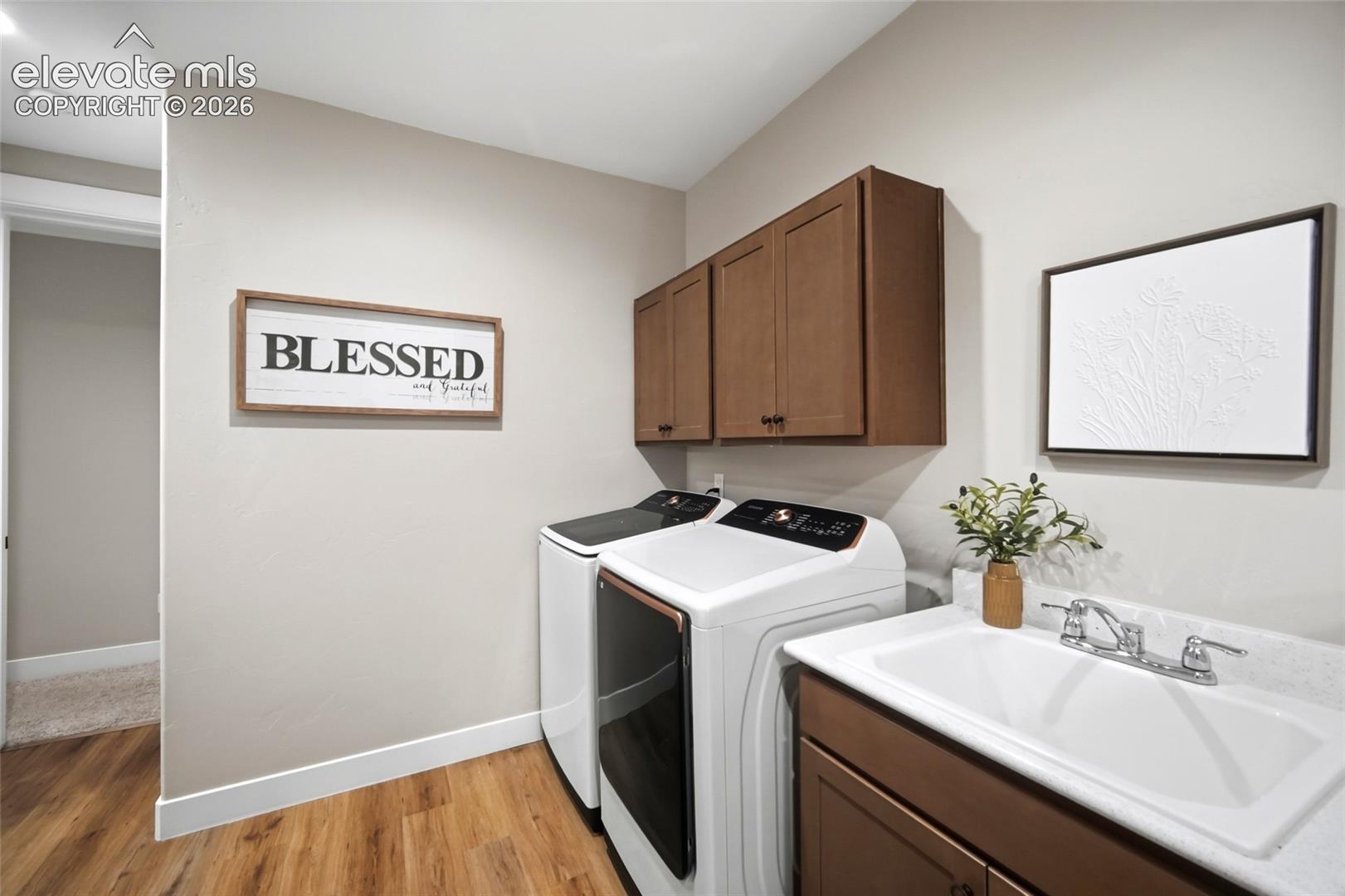 Laundry space featuring wood-finish cabinetry, a utility sink with a chrome dual-handle faucet, stone-finish countertop, and wood-finish flooring