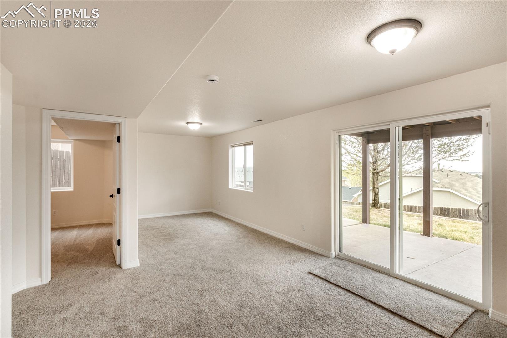 Spacious bonus room featuring neutral carpeting, recessed lighting, and a white sliding glass door leading to an outdoor patio.
