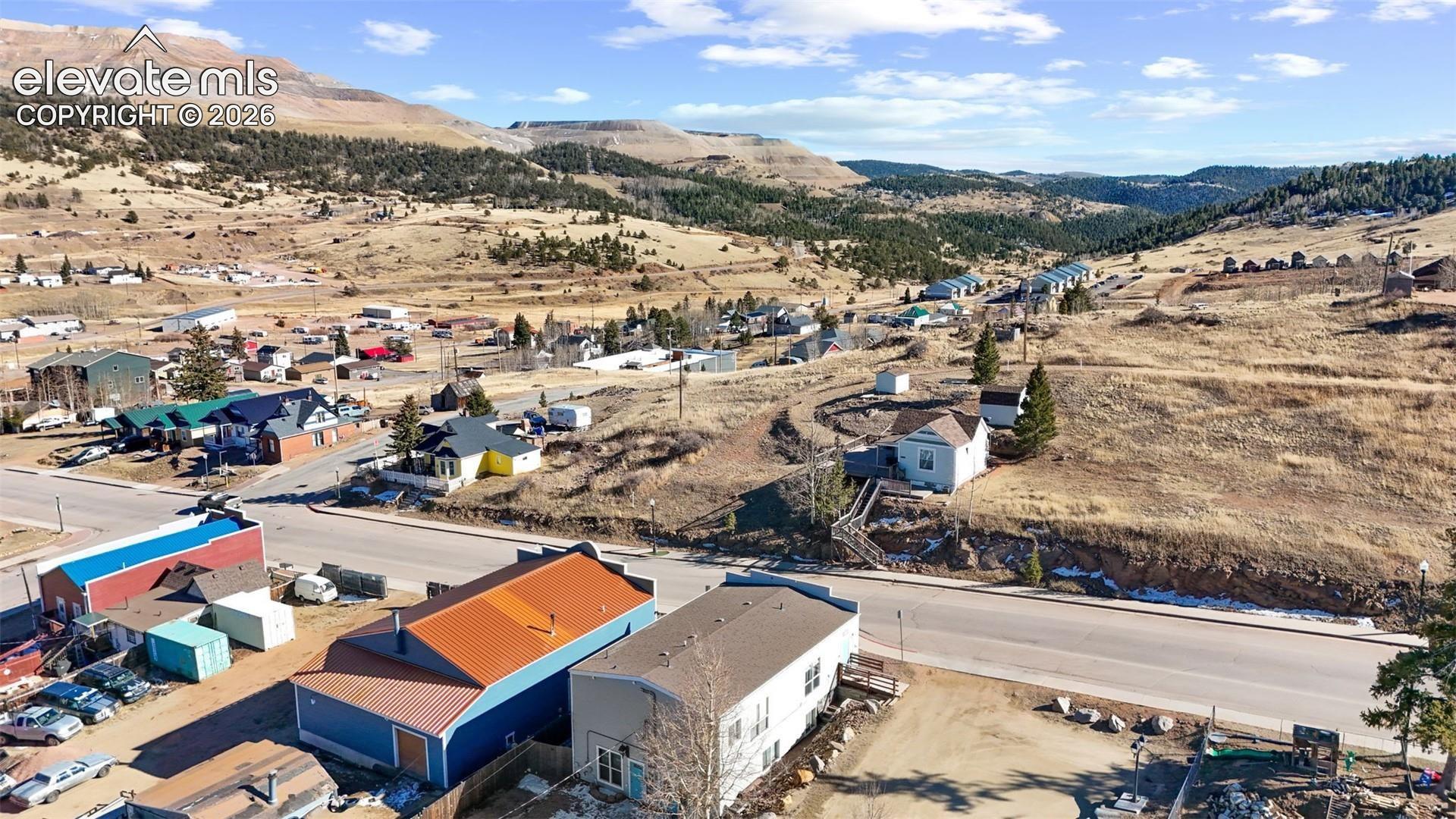 Aerial perspective of a multi-structure property featuring metal roof systems, expansive exterior terrain, and prominent mountainous topography