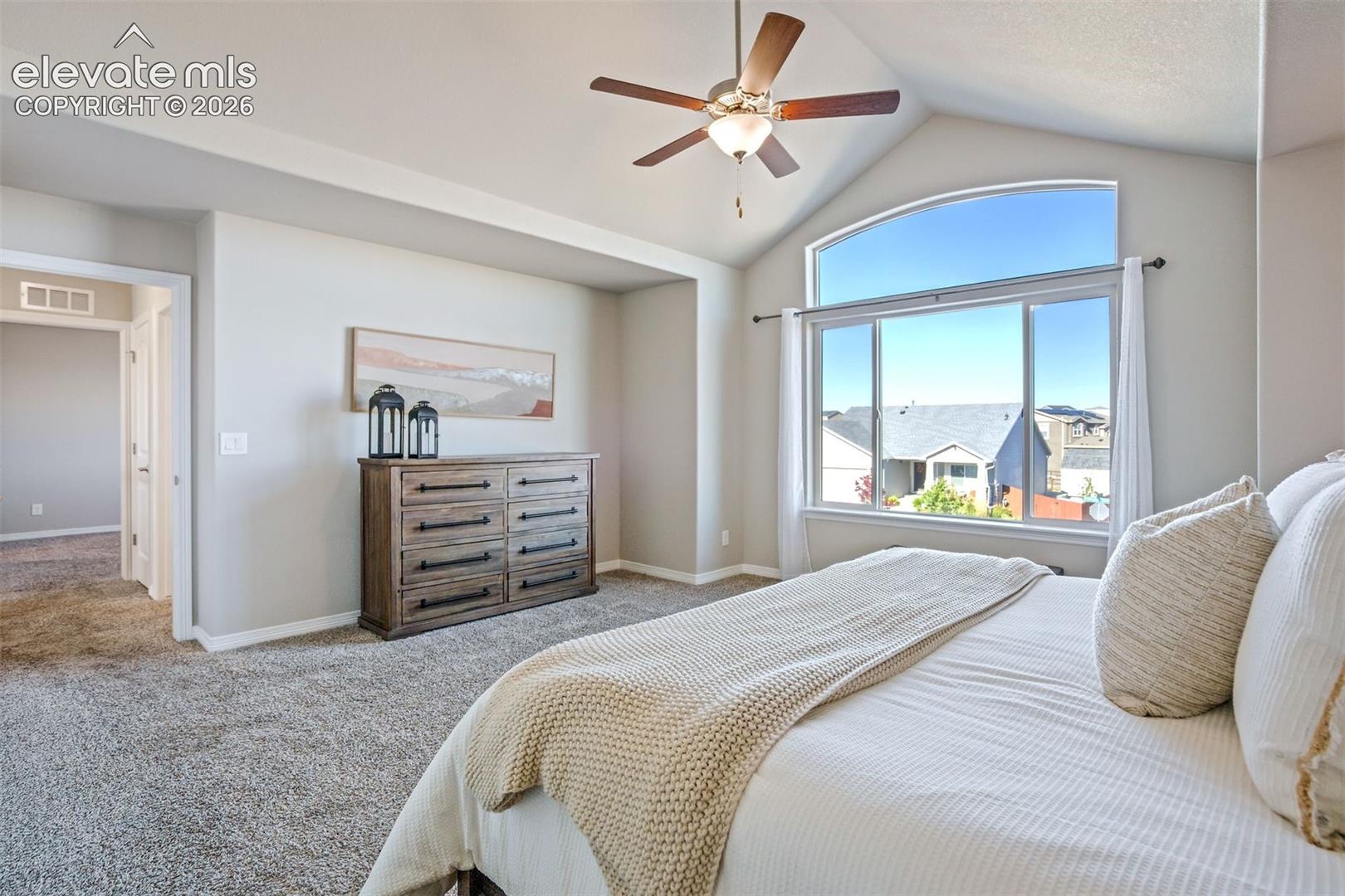 Vaulted ceiling featuring a ceiling fan, carpeted flooring, and a multi-pane window with an arched transom