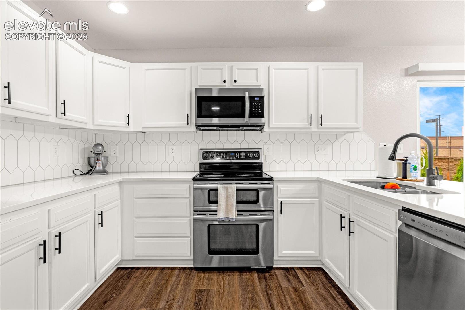 Kitchen featuring white shaker-style cabinetry, stainless steel appliances, white quartz countertops, geometric tile backsplash, and wood-finish flooring