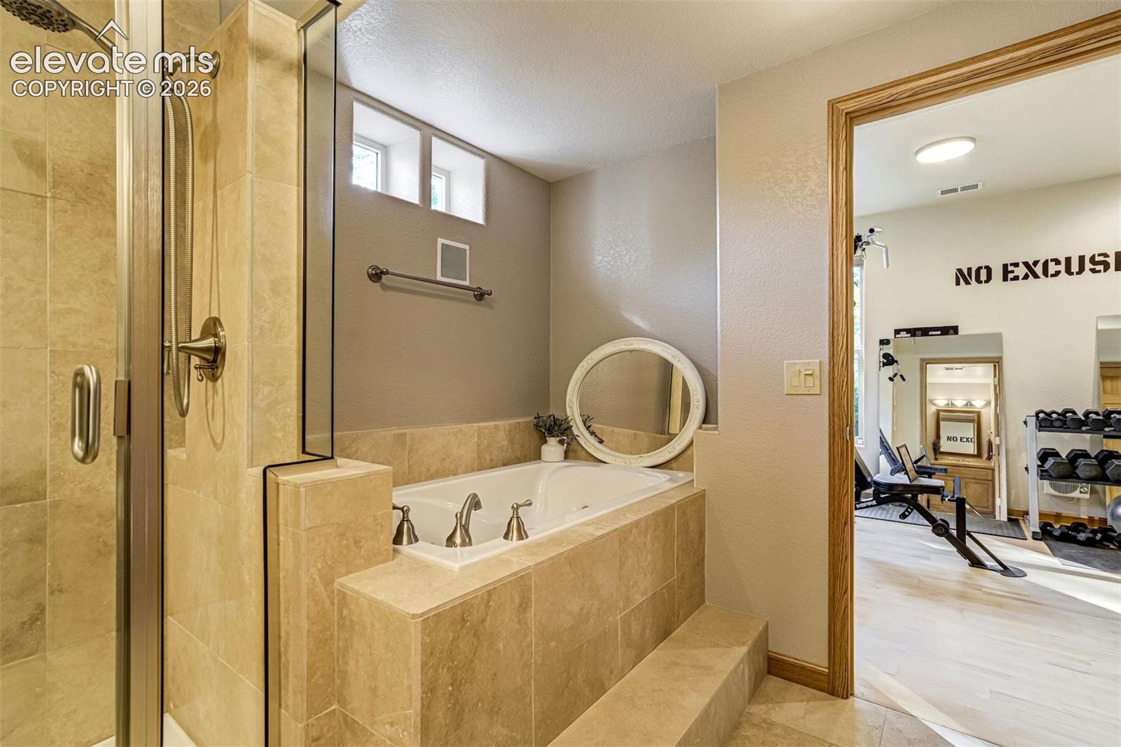 Tiled soaking tub with stepped surround, glass-enclosed shower, and translucent transom windows