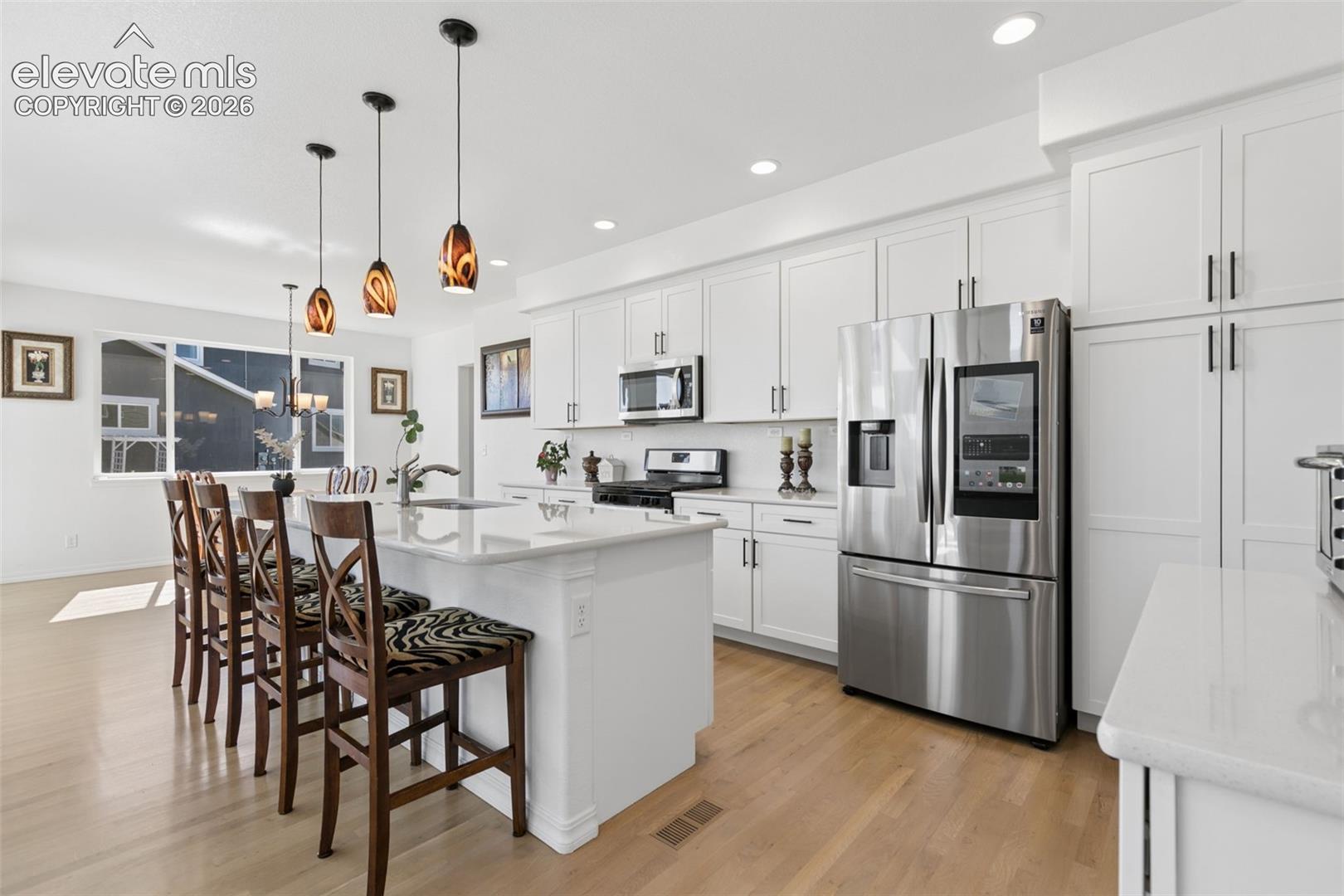 Kitchen featuring white cabinetry, stainless steel appliances, light wood-finish flooring, a center island with pendant lighting, and white countertops