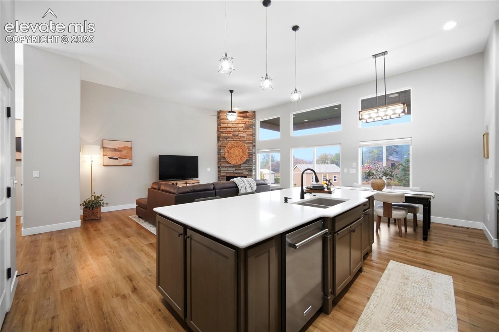 Kitchen featuring an island with a white countertop and dark cabinetry, wood-finish flooring, vaulted ceilings, stone-faced fireplace, and multiple windows