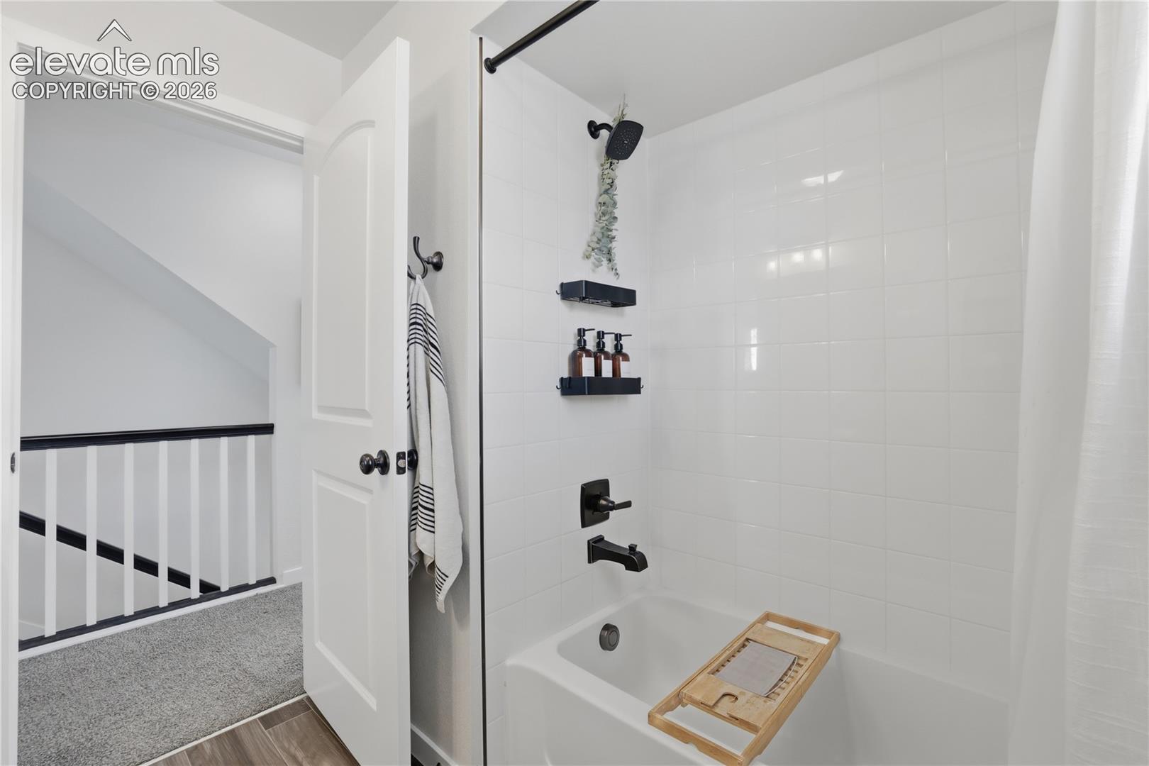 Bathtub and shower combination featuring white subway tile surround, matte black fixtures, and a white shower curtain