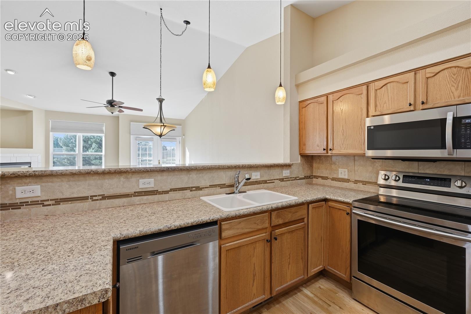 Kitchen featuring oak cabinetry, stone-finish countertops, stainless steel appliances, a double-basin sink, and multi-light pendant fixtures