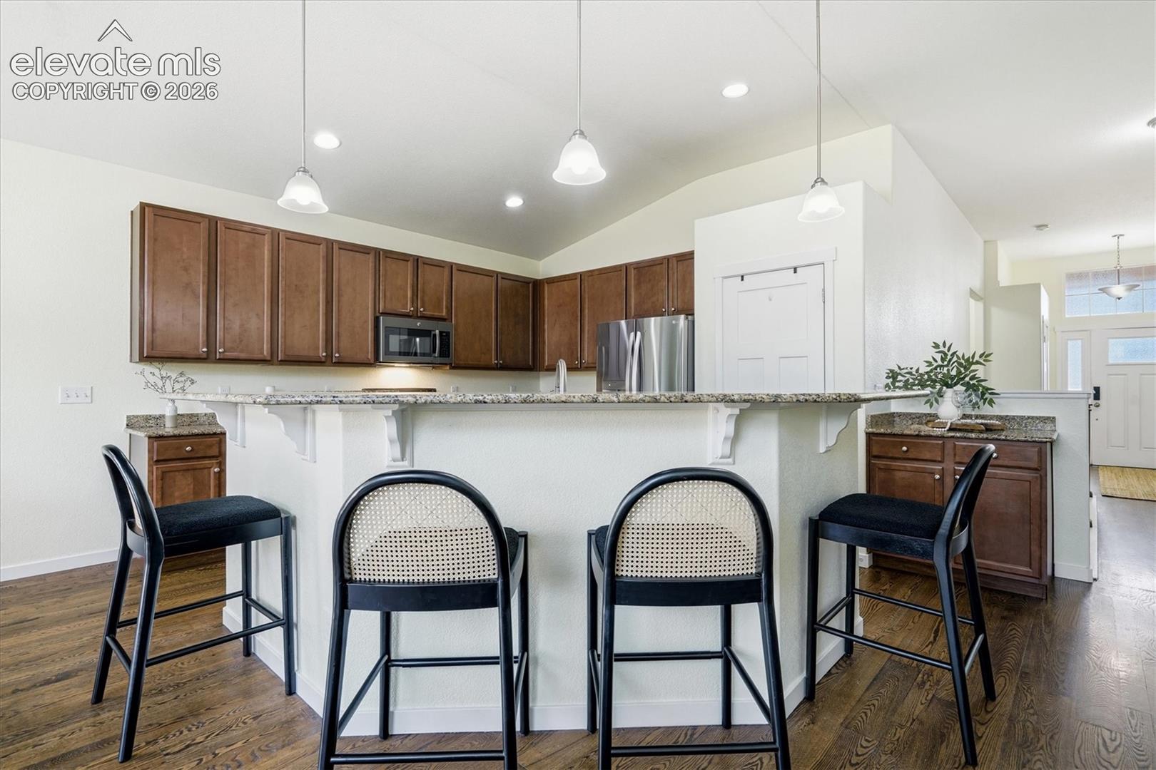 Kitchen featuring a breakfast bar with granite countertops, wood-finish flooring, dark wood cabinetry, and stainless steel appliances