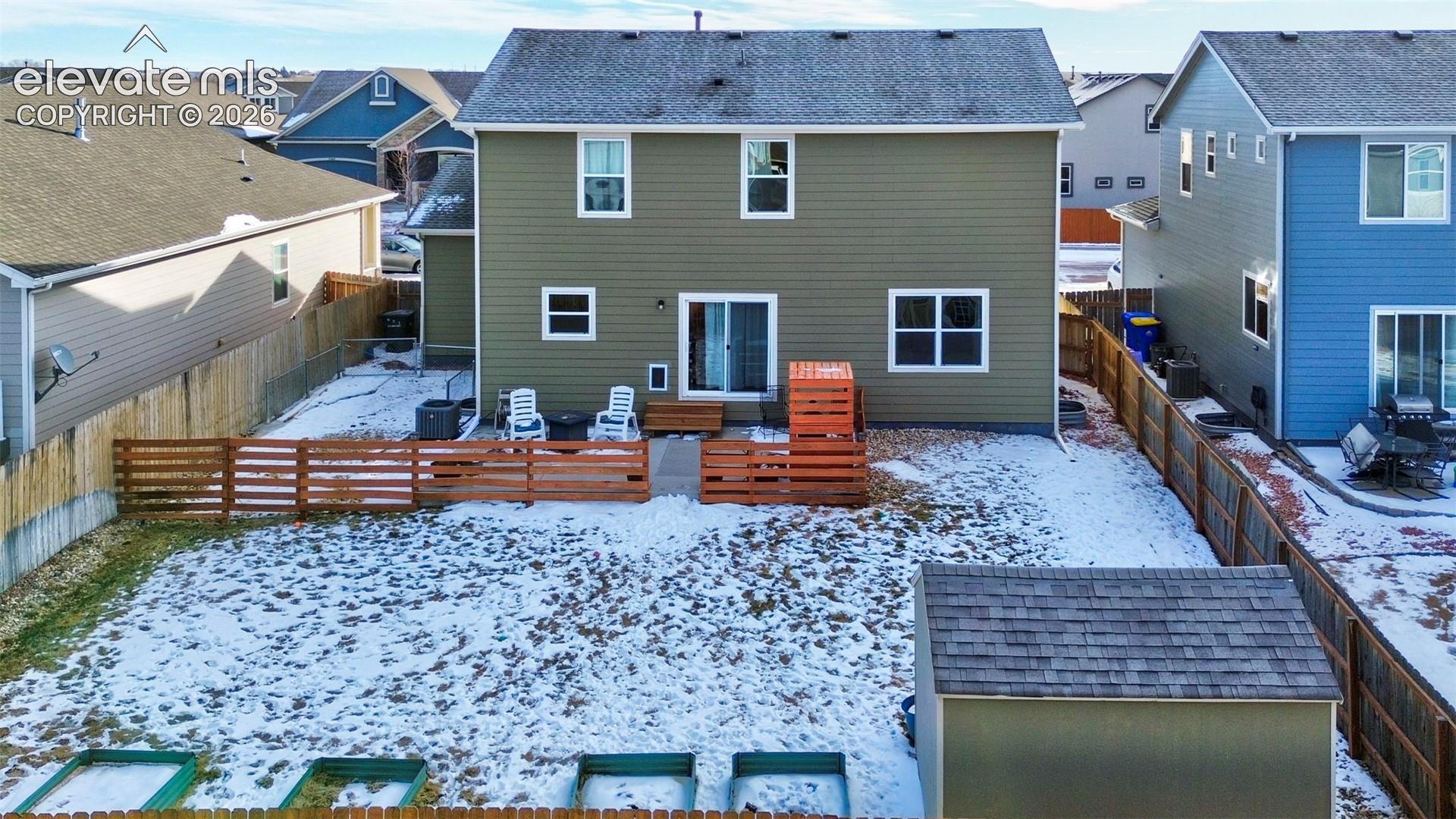 Two-story residence featuring green horizontal siding, asphalt shingle roof, rear patio, perimeter wood fencing, and a detached storage structure