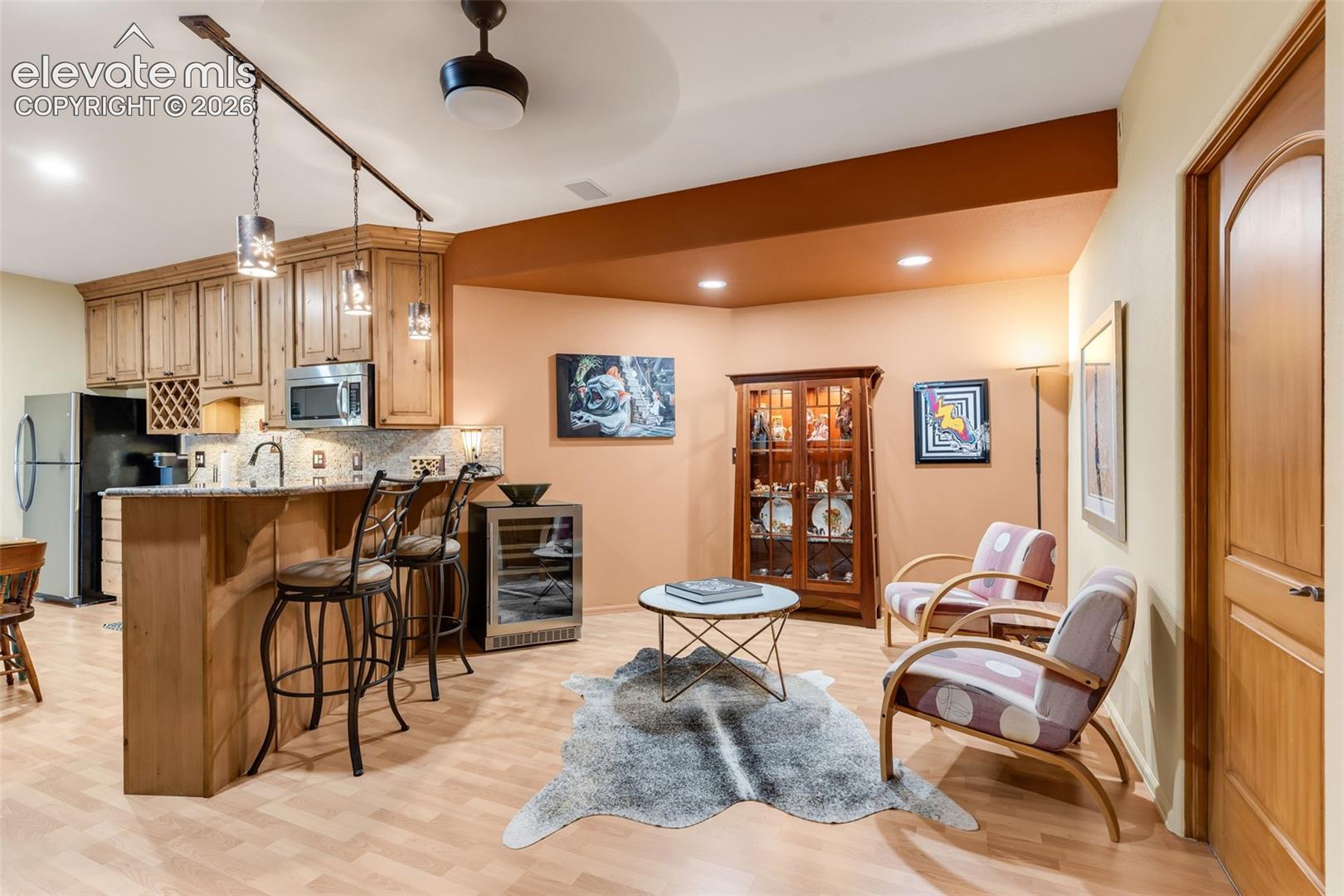 Kitchen featuring light-tone wood cabinetry, stone-finish countertops, built-in wine refrigerator, pendant lighting, and wood-finish flooring