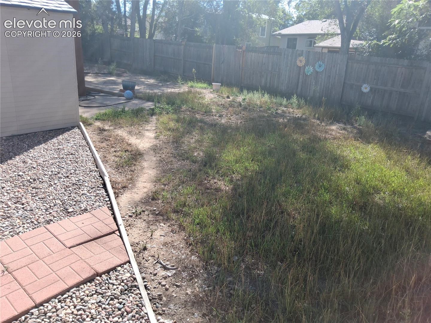 Backyard featuring wood fencing, a stone-paver walkway, gravel hardscaping, and a detached exterior structure